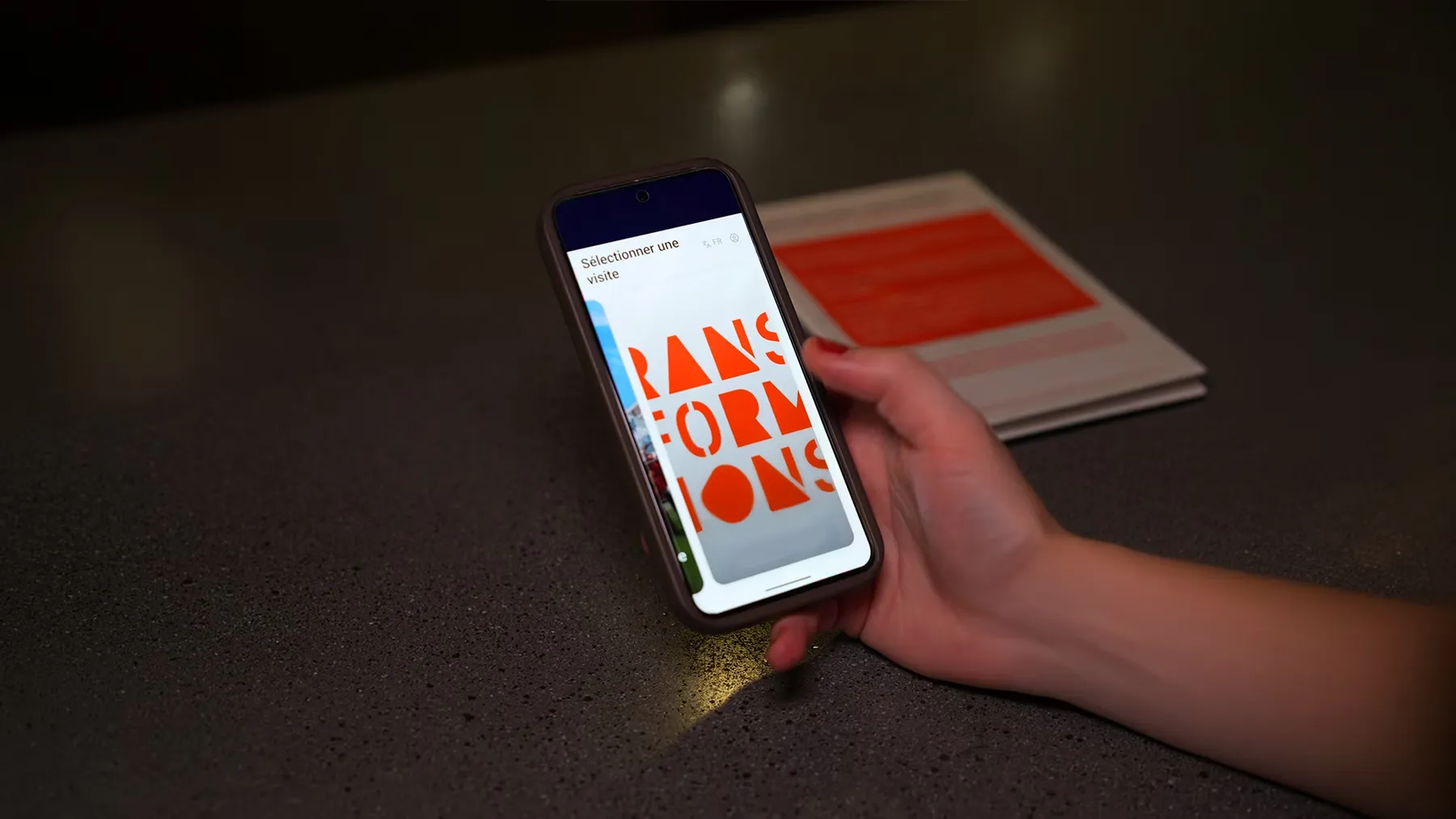 A visitor choosing a route on their phone in a dark gallery